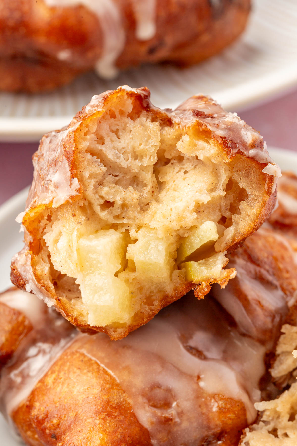 Close-up of a gluten-free apple fritter with a bite taken out, showing a fluffy interior filled with apple chunks and topped with a light glaze.