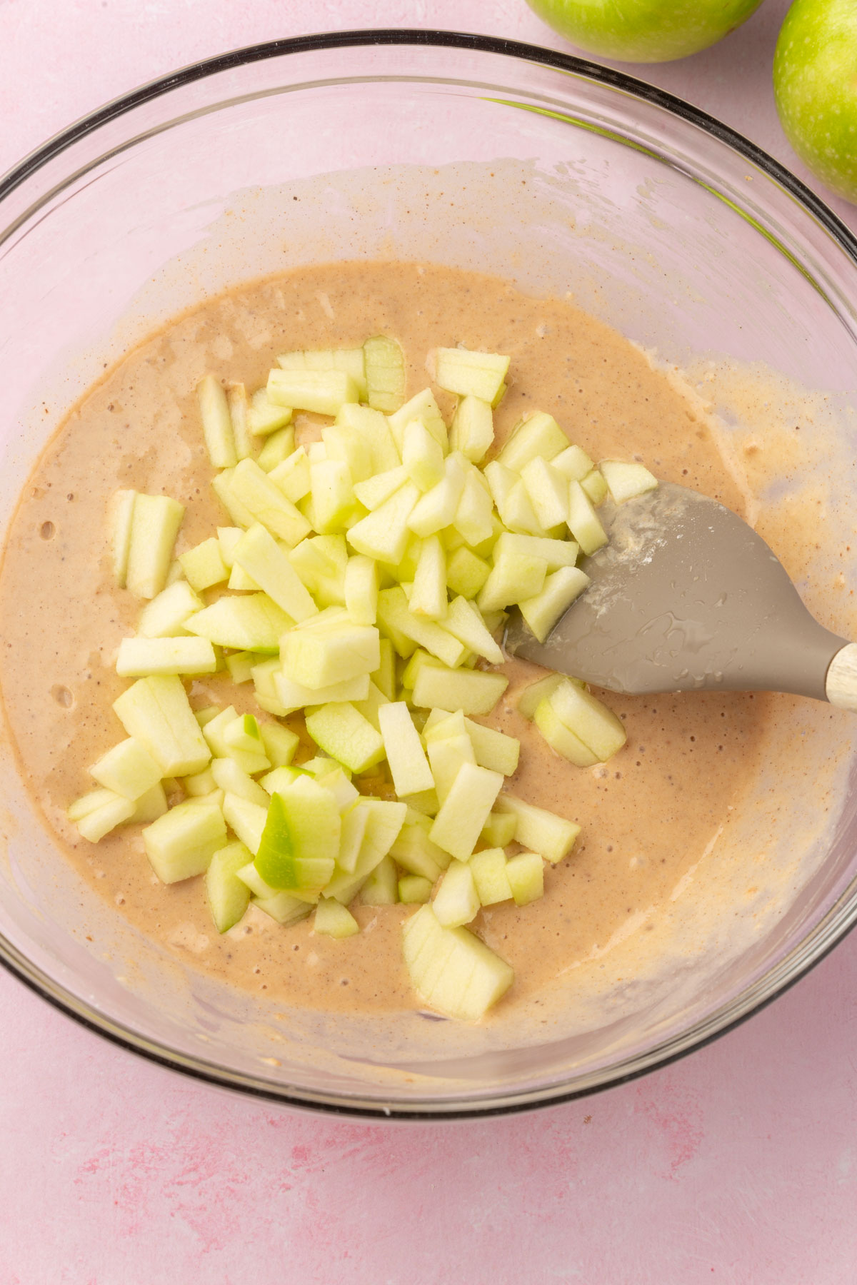A glass mixing bowl with gluten-free apple fritter batter topped with diced granny smith apple before mixing together.