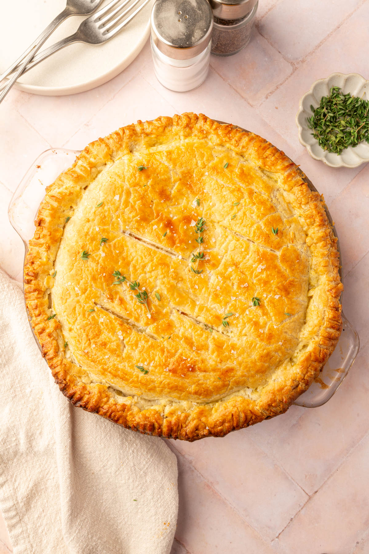 Finished gluten-free chicken pot pie with fresh thyme garnish resting on a brick countertop.