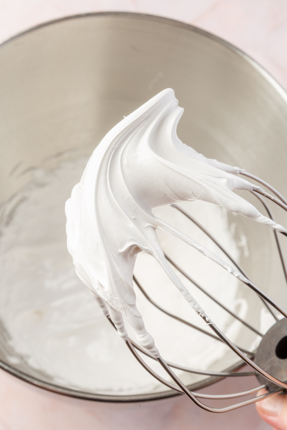 A close-up of a metal whisk with stiff marshmallow meringue peaks, highlighting the fluffy and smooth texture.
