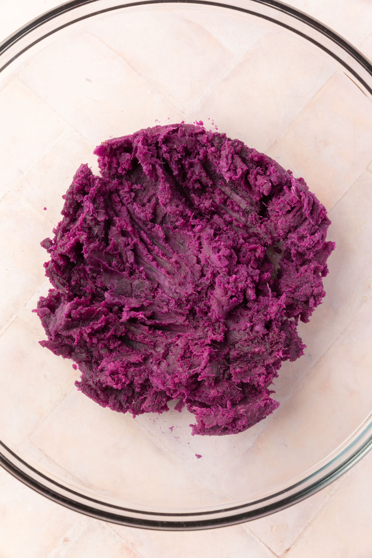 Mashed purple sweet potato in a clear glass bowl, showing the vibrant purple color and smooth texture.