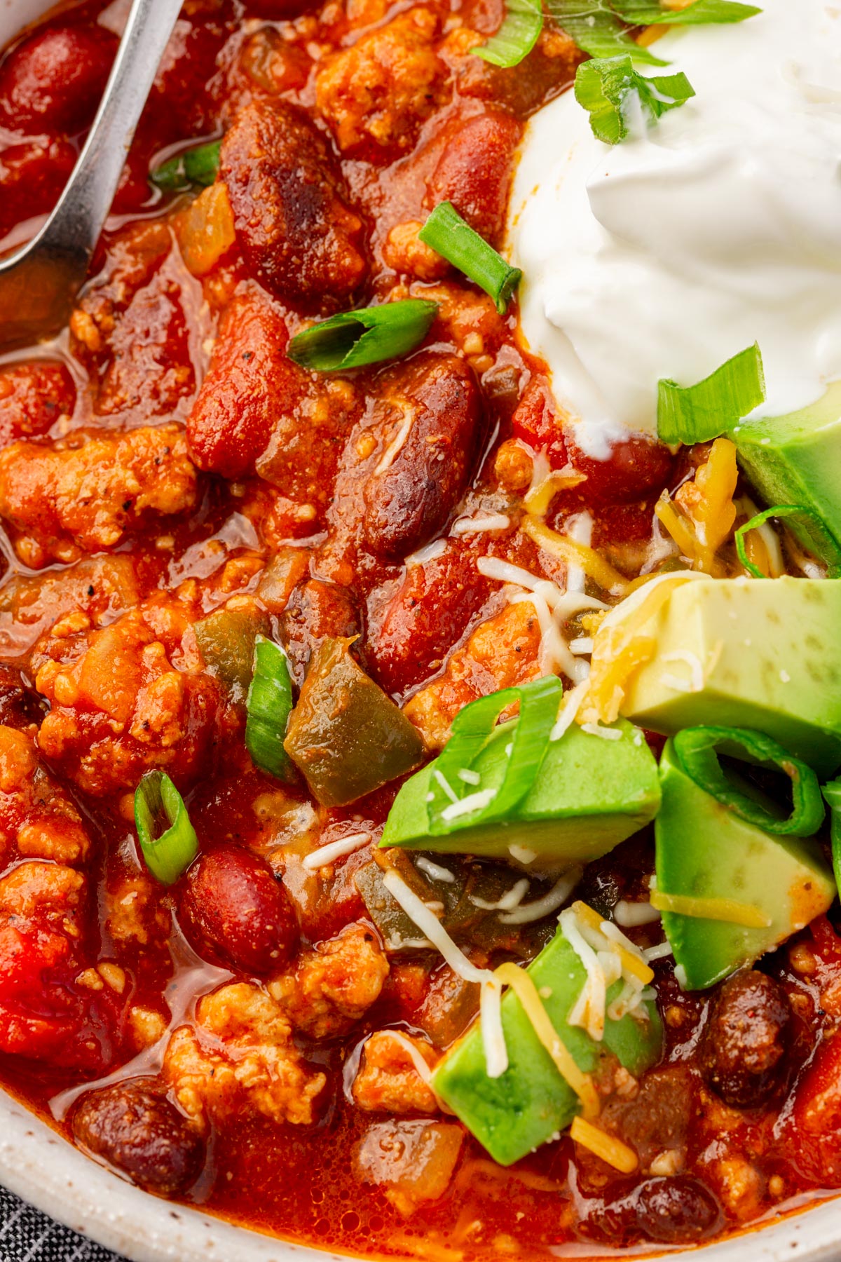 Close up image of finished slow cooker turkey chili with cheese, avocado, green onion and sour cream garnish.