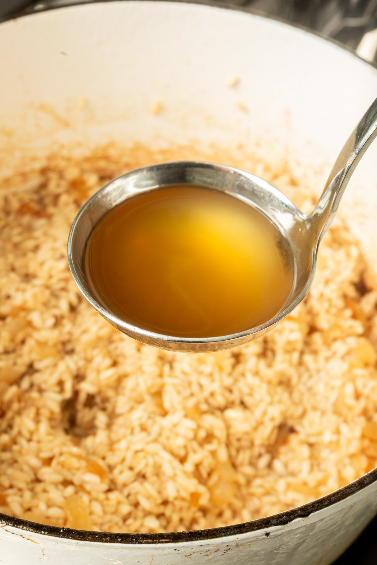 Ladle of vegetable broth above a large pot of arborio rice mixture.