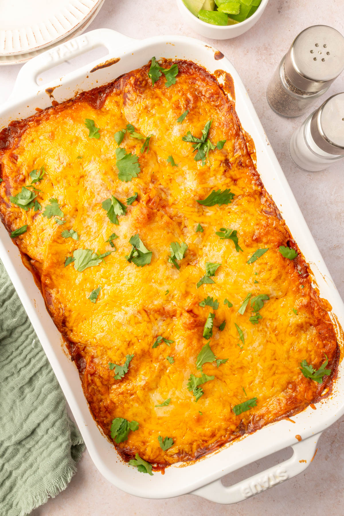 Large white baking pan of finished chicken enchilada casserole with cilantro on top.