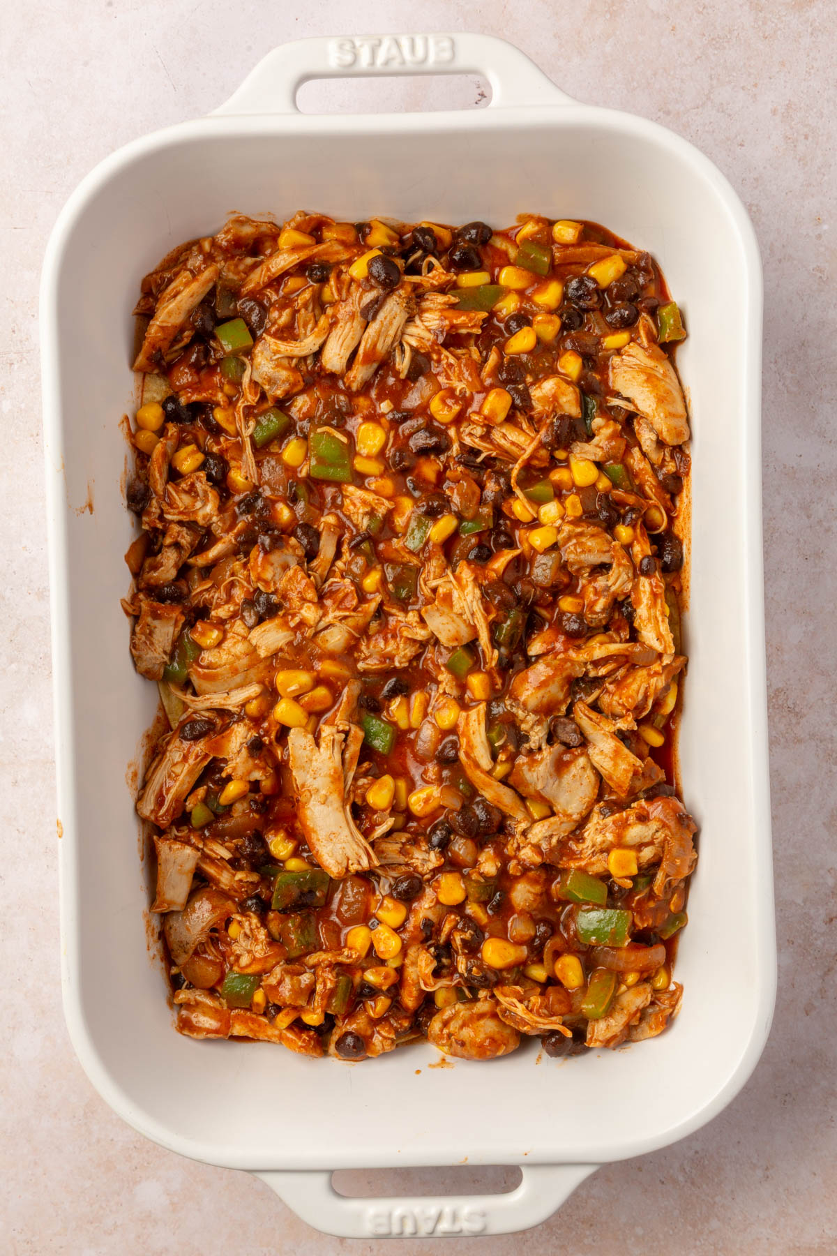 Large white baking pan with first layer of chicken enchilada mixture in bottom of the pan.