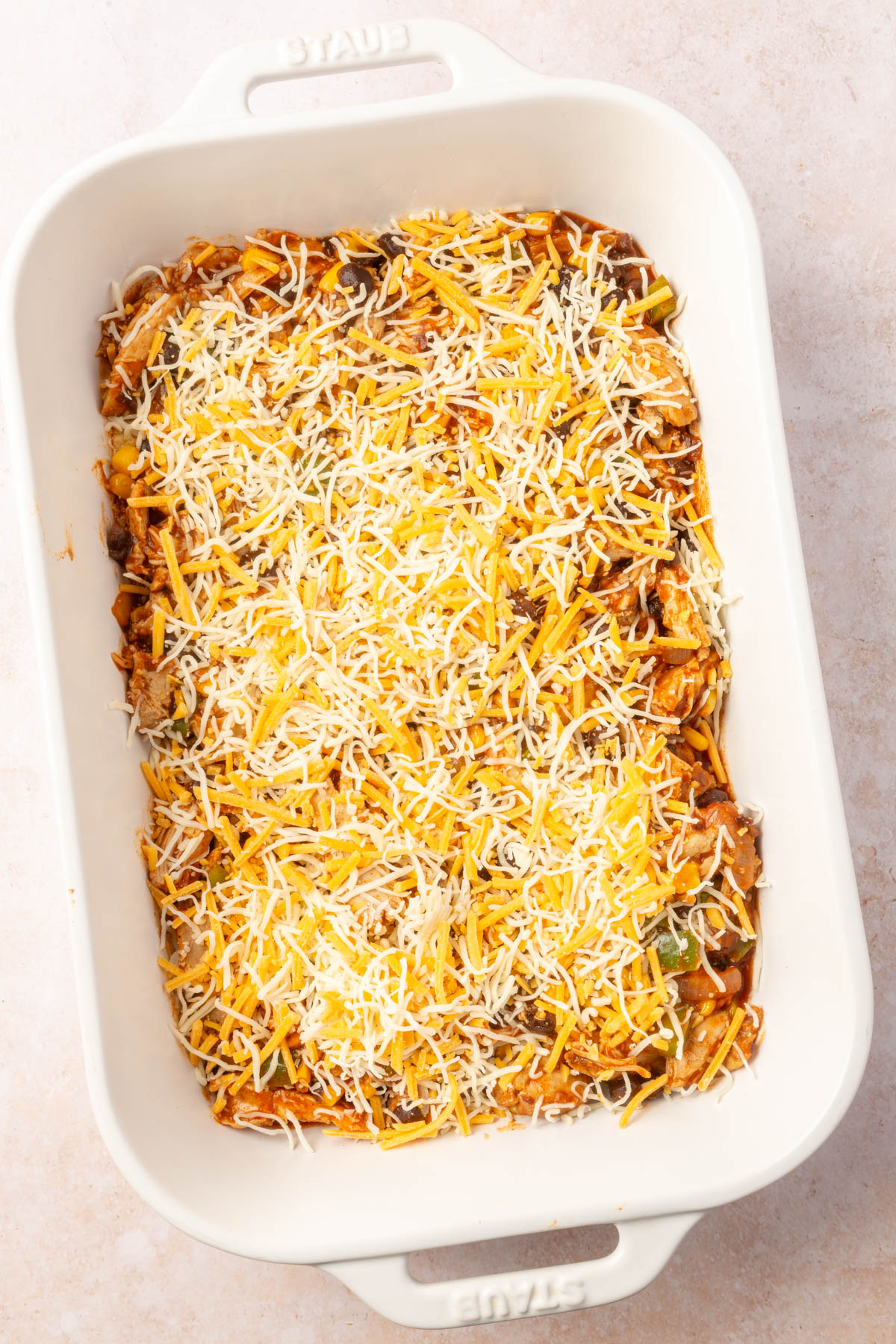 Large white baking pan with first layer of chicken enchilada mixture in bottom of the pan with cheese on top.