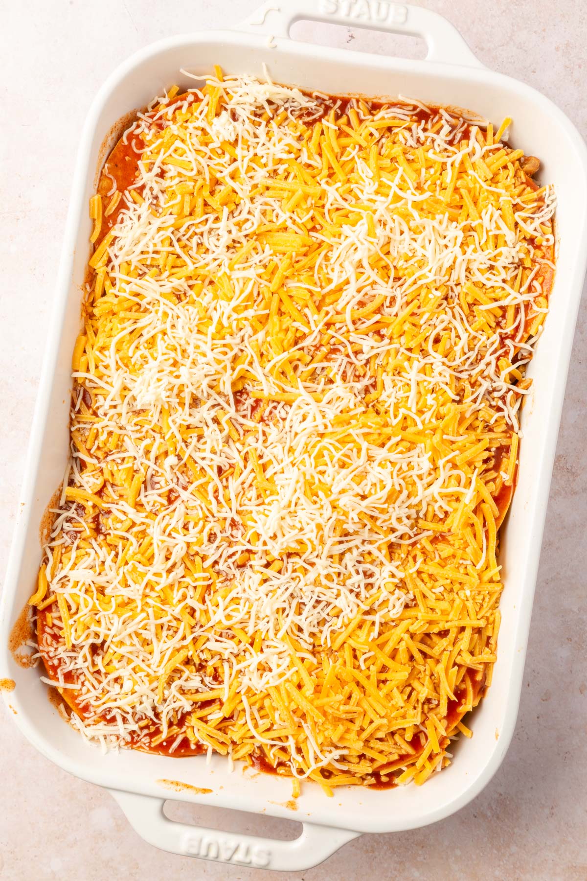 White baking pan with chicken enchilada casserole mixture in it with cheese sprinkled on top, before cooking.