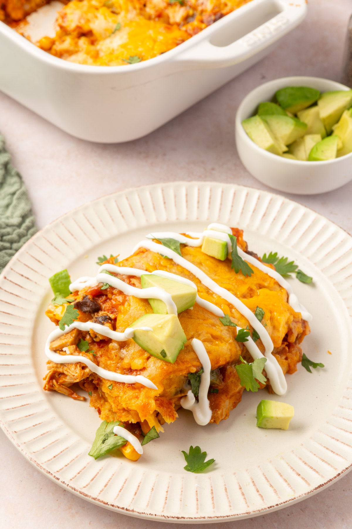 Image of a slice of chicken enchilada casserole with avocado, cilantro and sour cream drizzle on top.