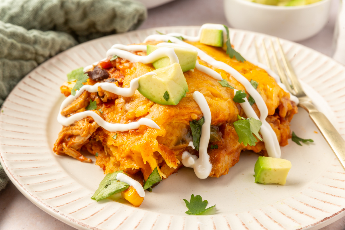 Close up image of a slice of chicken enchilada casserole with avocado, cilantro and sour cream drizzle on top.