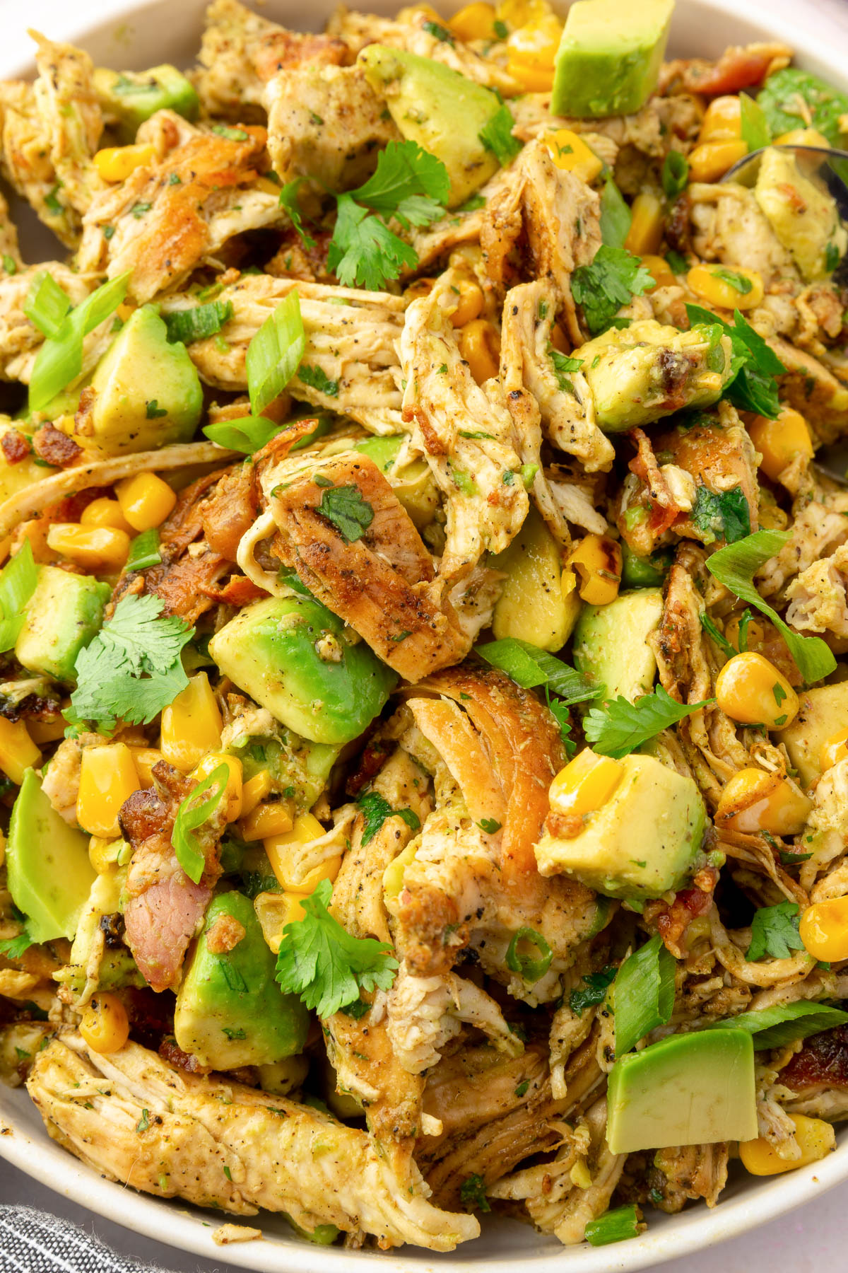 A close of up avocado chicken salad in a bowl with corn and cilantro.