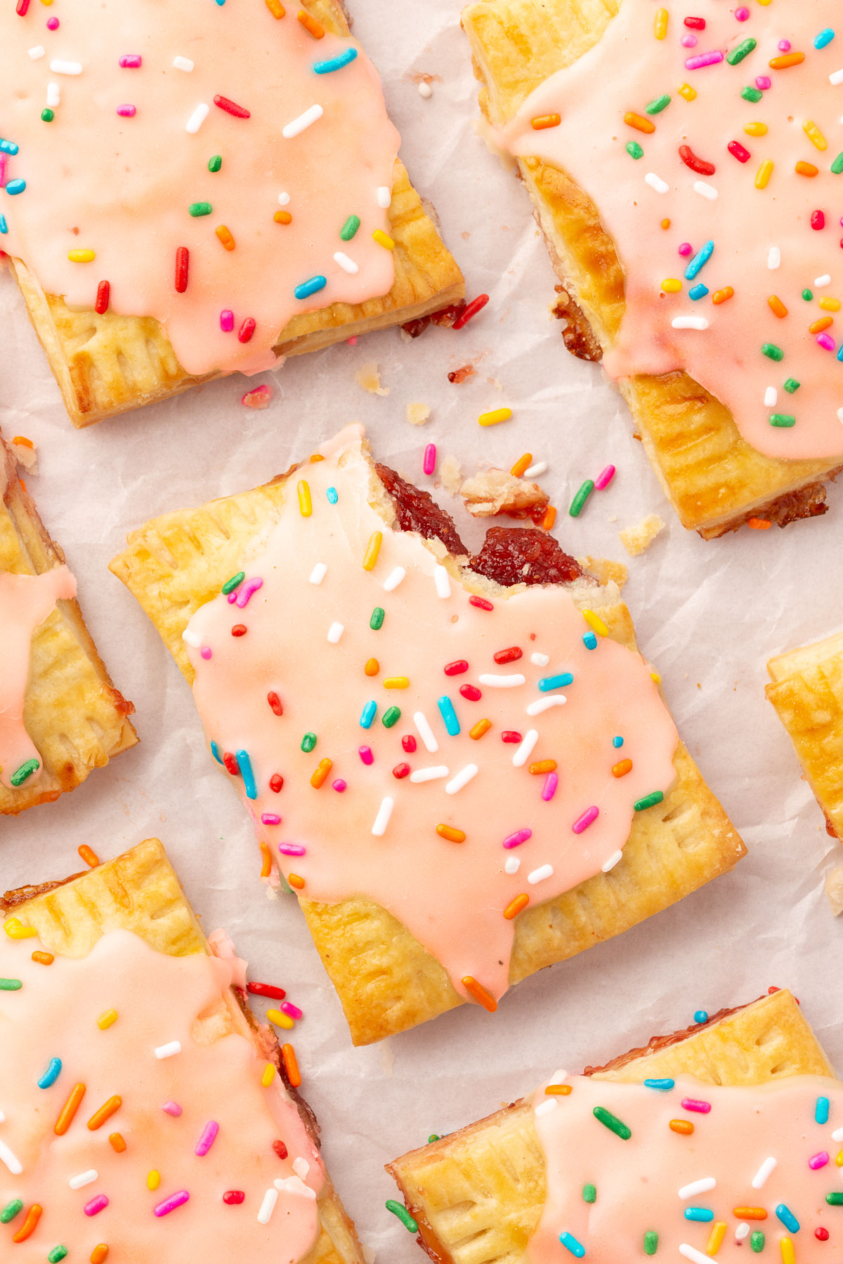 Image of finished gluten-free pop tarts laying on parchment paper with a corner of one of the pop tarts broken off.
