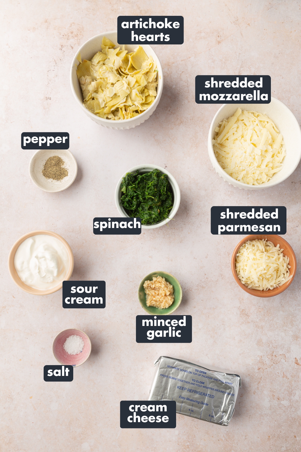 Ingredients for spinach artichoke dip including: artichoke hearts, shredded mozzarella, shredded parmesan, spinach, pepper, sour cream, minced garlic, cream cheese and salt.