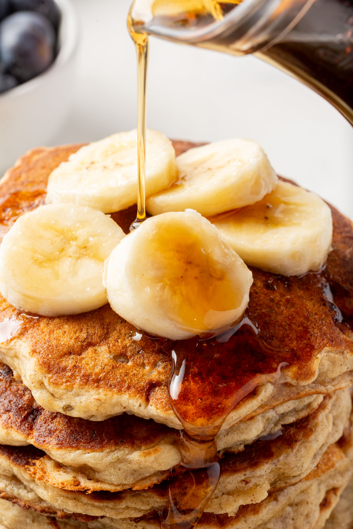 Close-up of maple syrup being poured over banana slices on top of gluten-free banana pancakes.