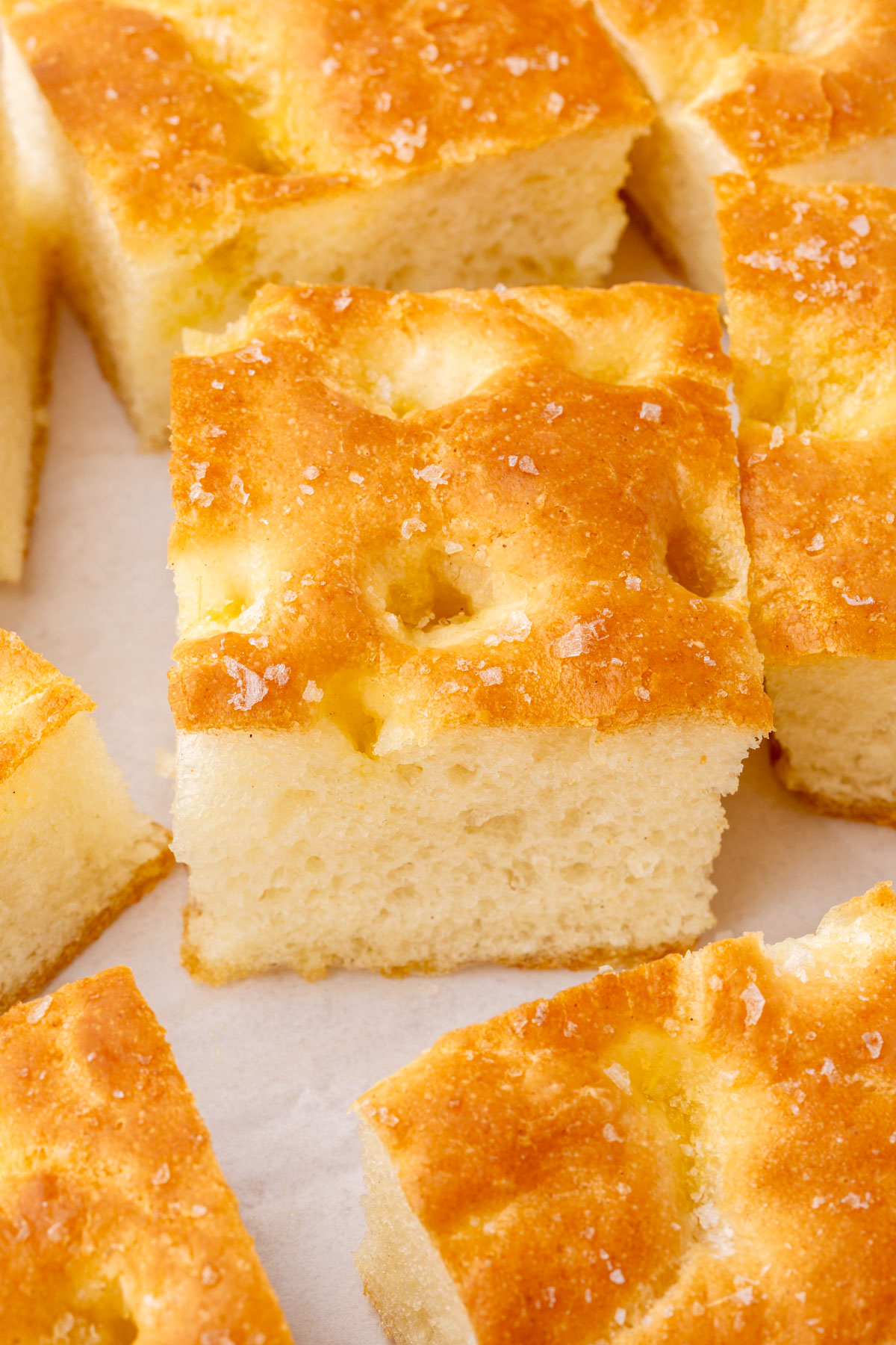 Extreme close-up of the dimpled top and open crumb structure of a slice of gluten-free focaccia with visible sea salt crystals.