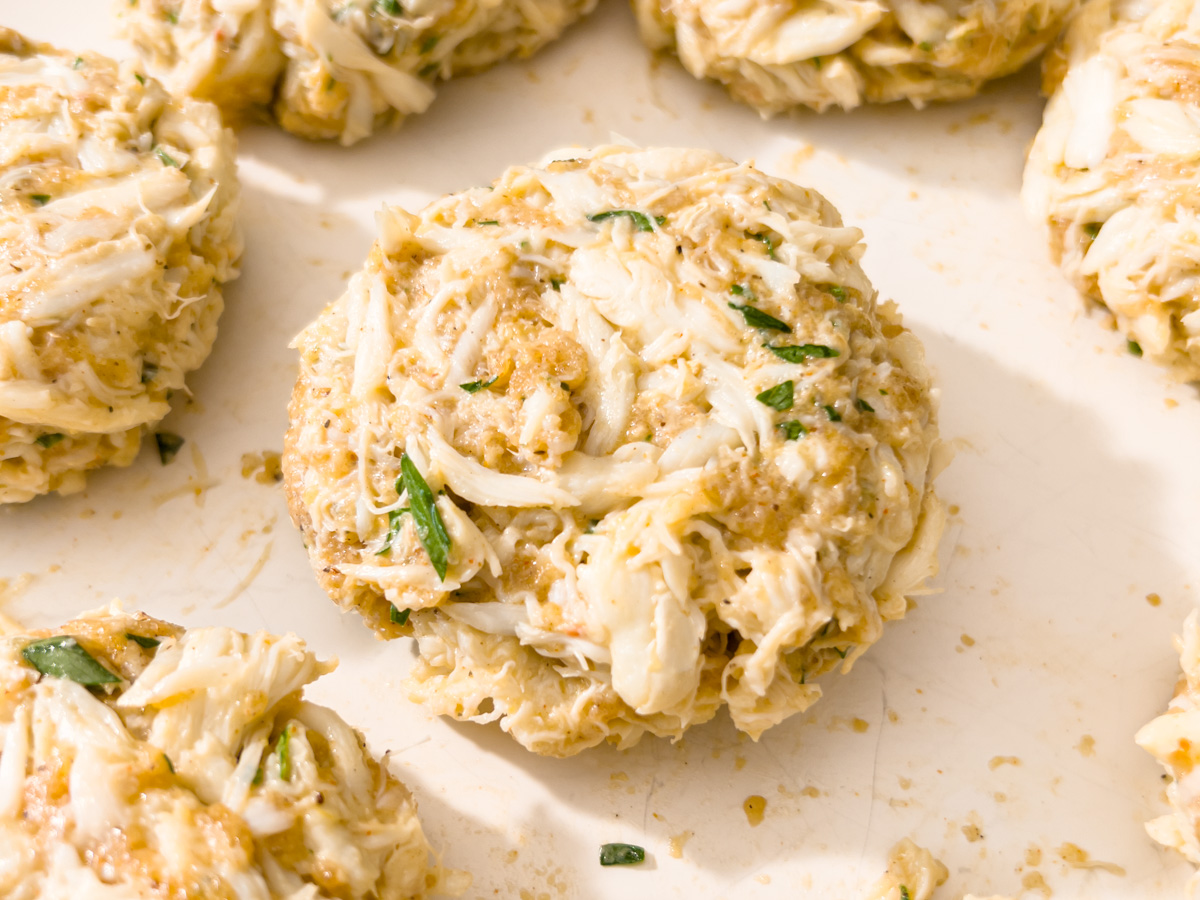 Close-up of a raw gluten-free crab cake patty on a white surface before frying.