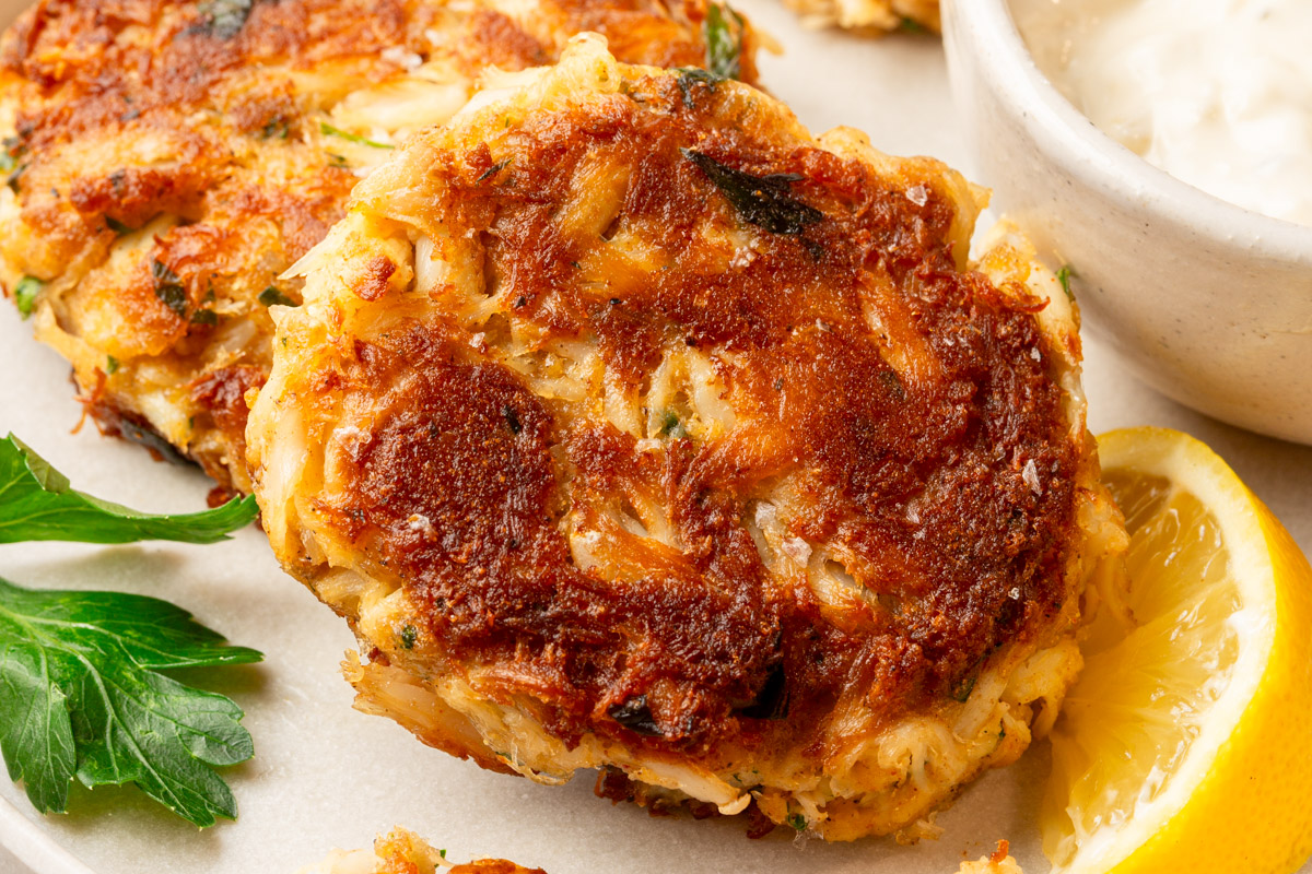 Crispy gluten-free crab cake on a plate with parsley garnish and a lemon wedge.