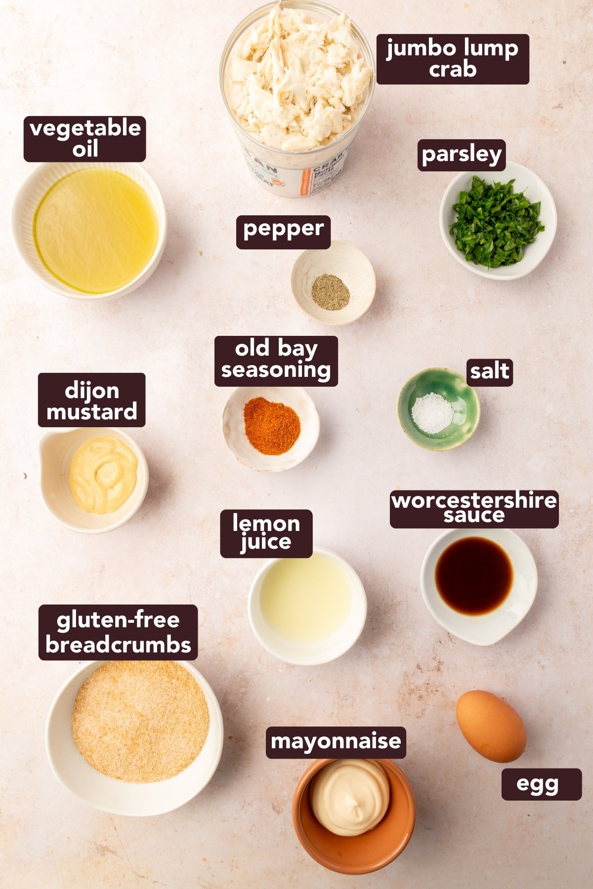 Overhead view of labeled ingredients for gluten-free crab cakes including jumbo lump crab, Old Bay seasoning, gluten-free breadcrumbs, and egg.