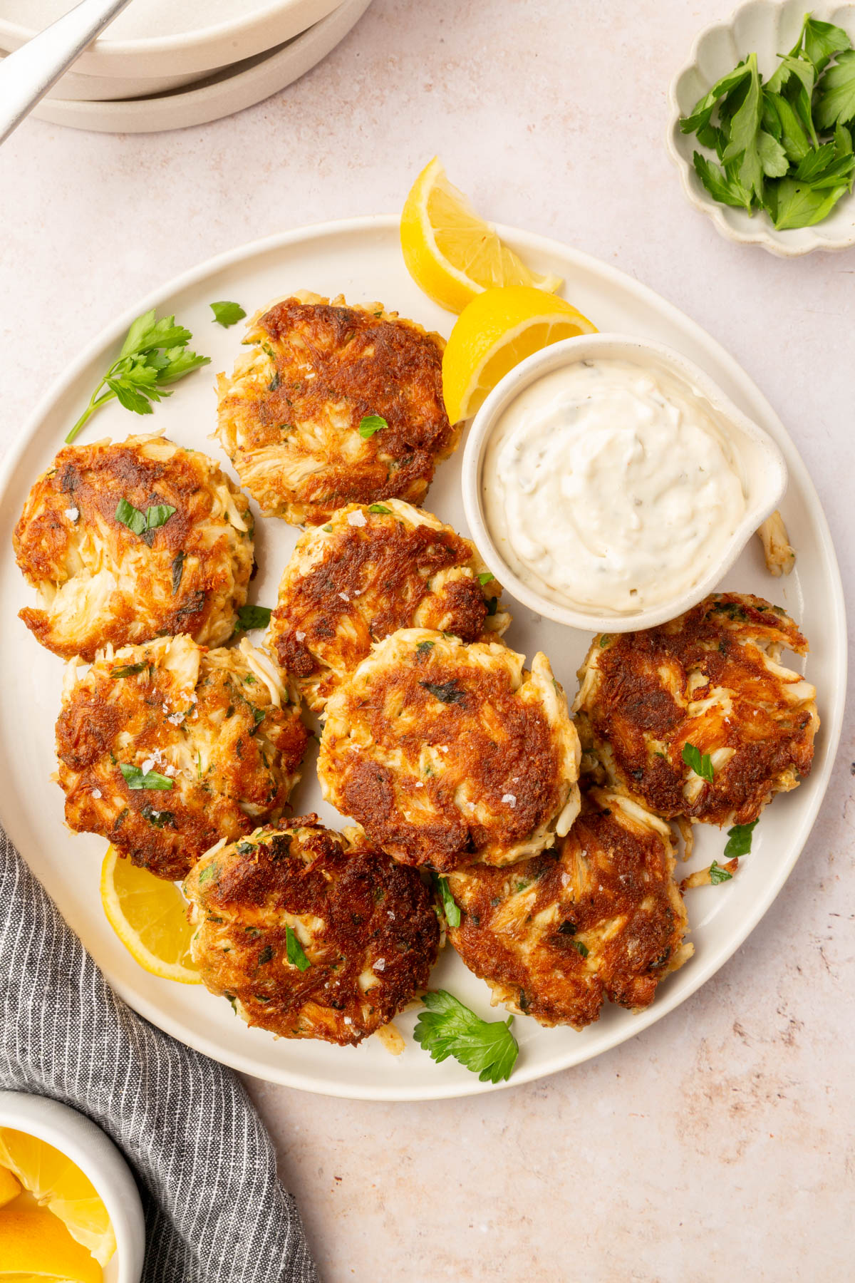 Full plate of gluten-free crab cakes arranged around a bowl of tartar sauce with lemon wedges and parsley