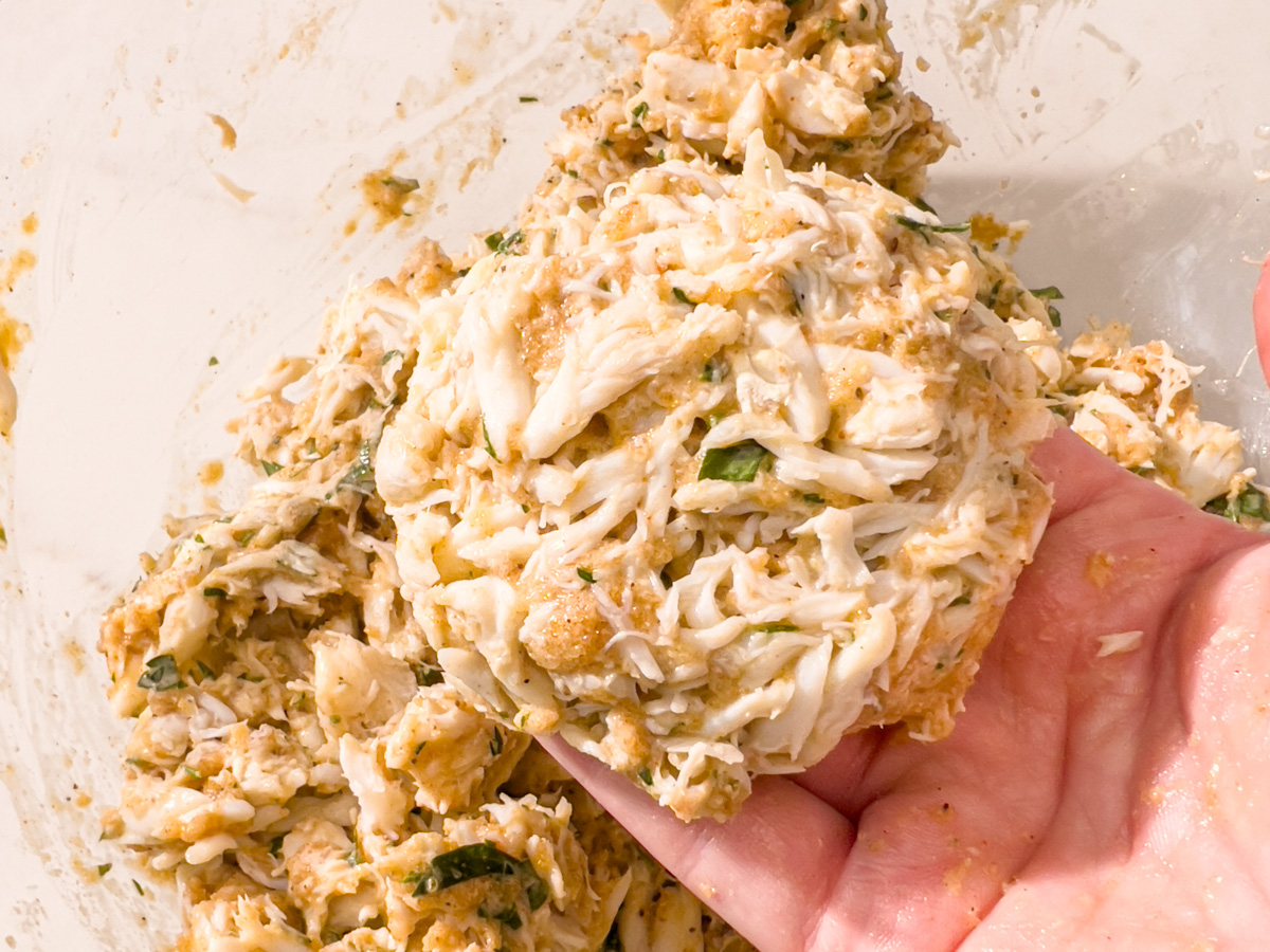 Uncooked gluten-free crab cake patty held in one hand before frying.