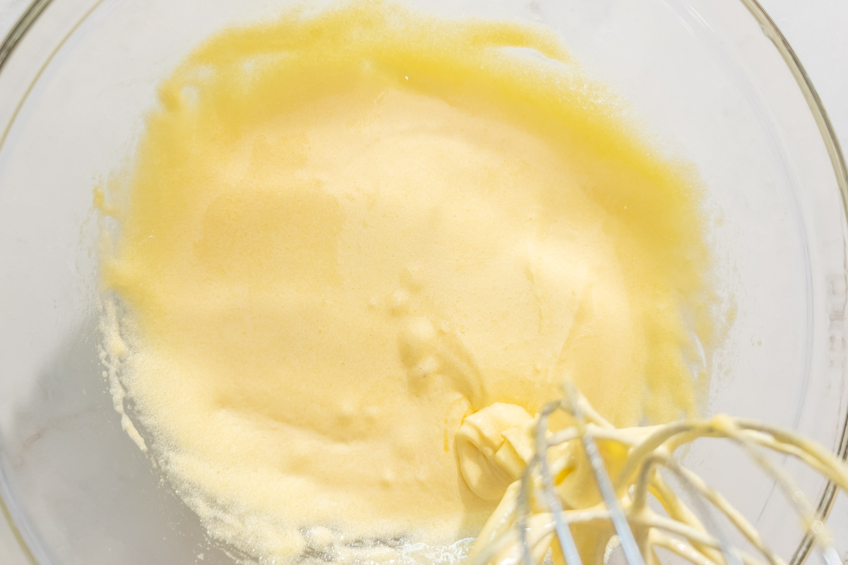 Whisked egg yolks and sugar mixture in a glass bowl, showing a pale yellow and smooth texture.
