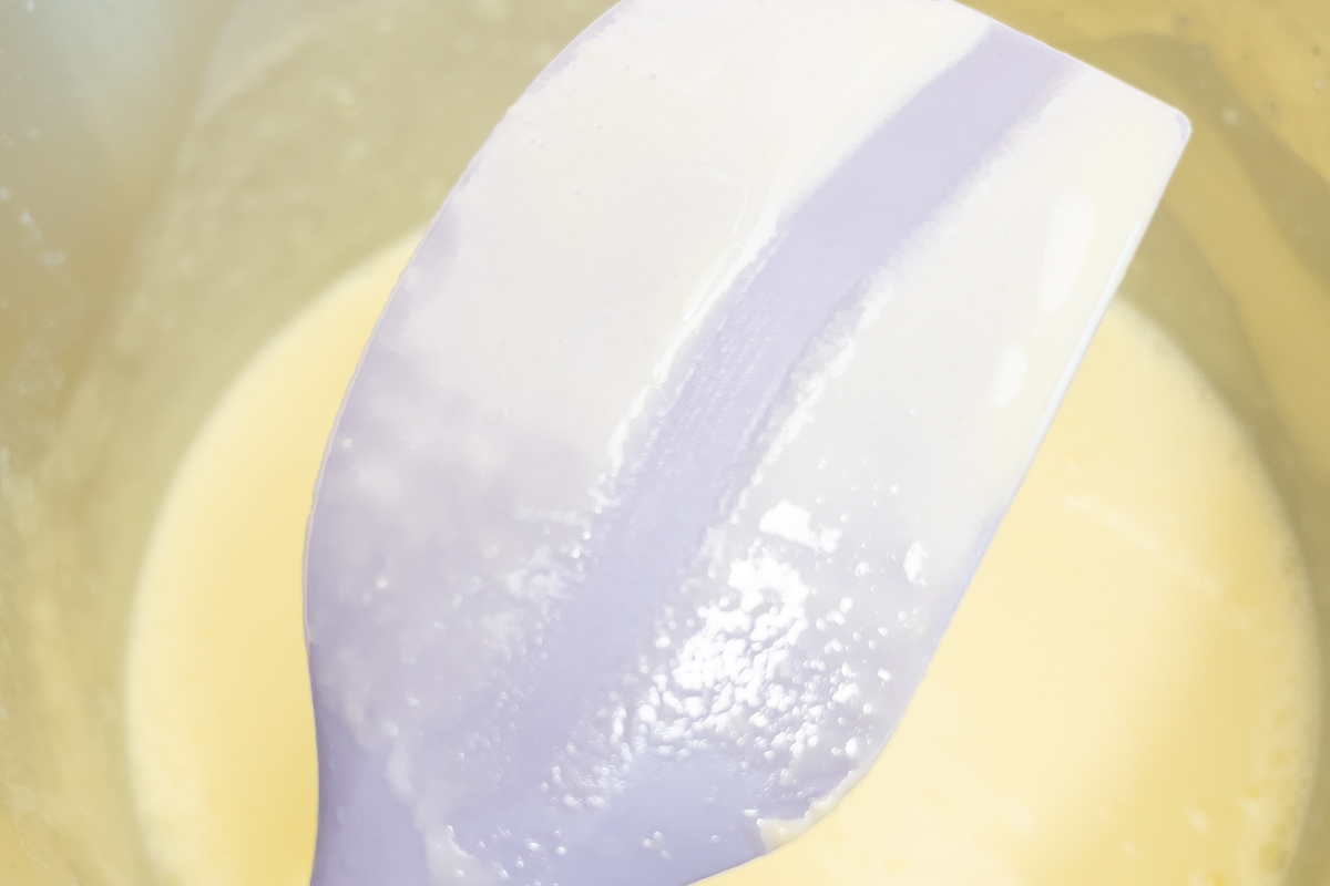Purple spatula coated with cooked custard, demonstrating proper consistency for ice cream base.