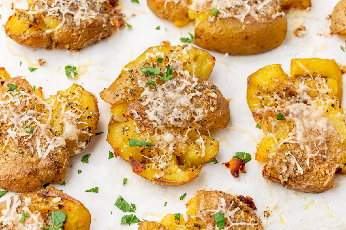 Parmesan smashed potatoes roasted on parchment-lined baking sheet with golden crispy edges.