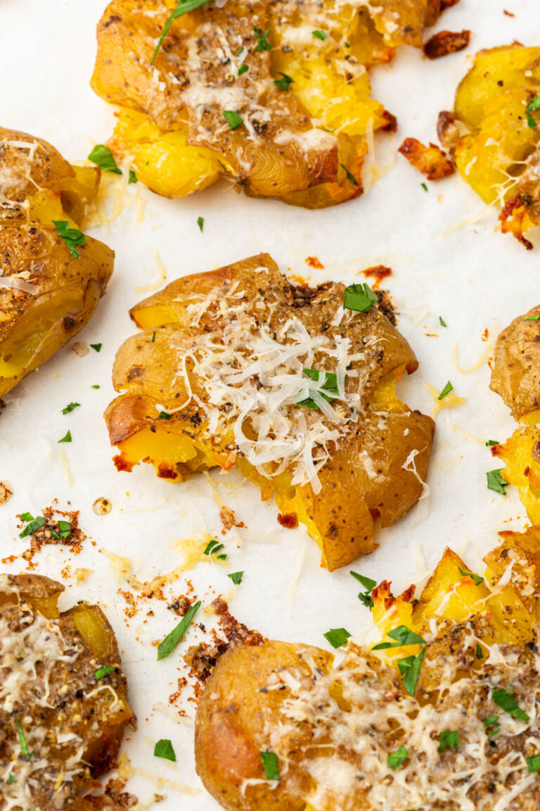 Close-up of a single smashed potato topped with melted parmesan and fresh parsley.