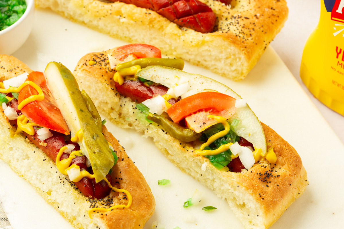 Close-up of a Chicago-style gluten-free hot dog focaccia slice topped with pickle, tomato, onion, and mustard.