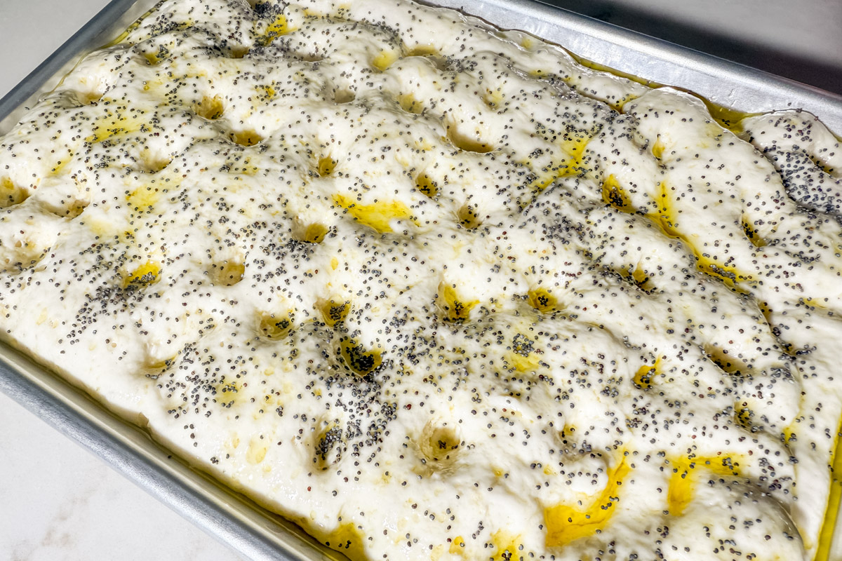 Gluten-free focaccia dough sprinkled with poppy seeds and olive oil just before baking.