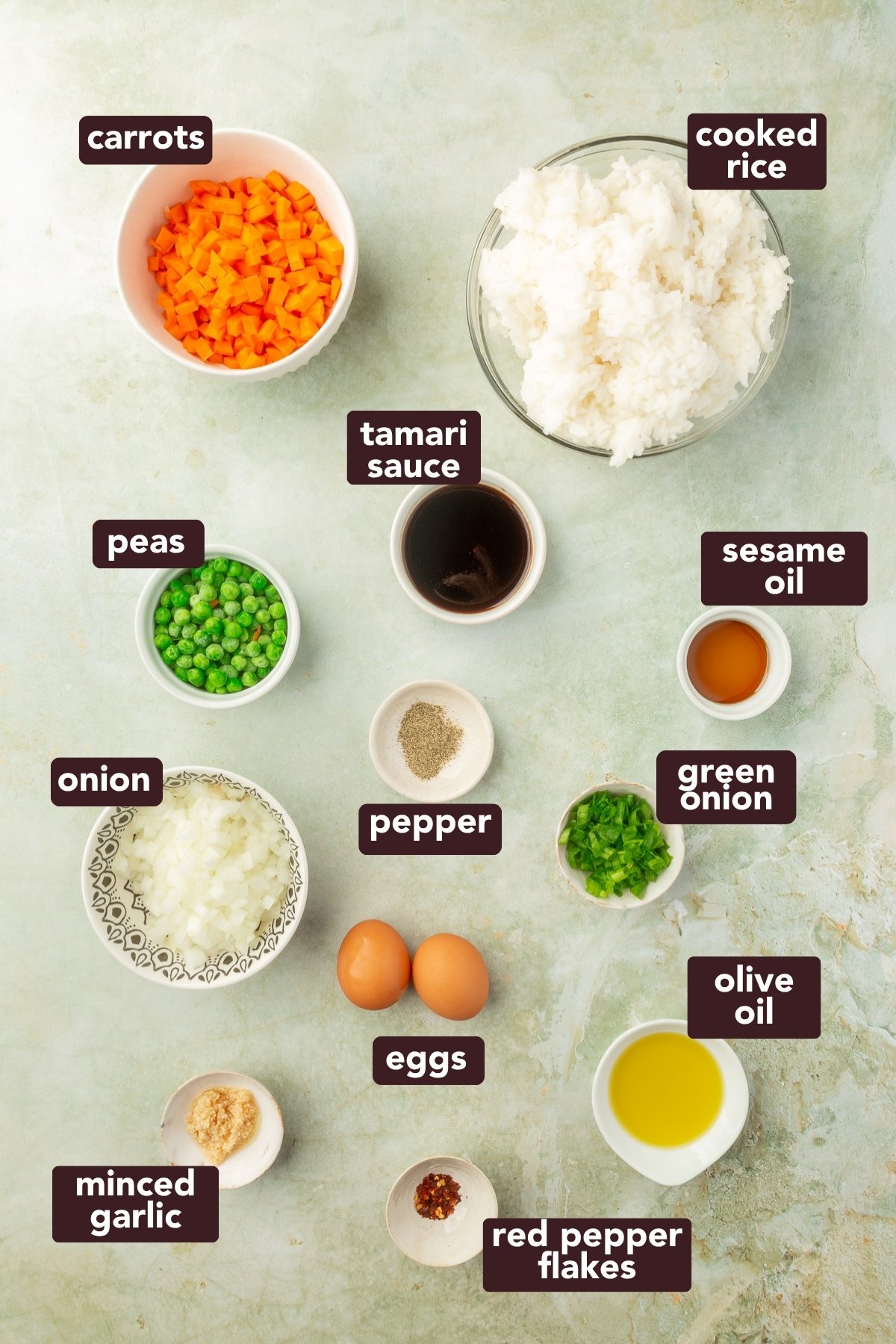 Overhead view of ingredients for gluten-free fried rice including rice, carrots, peas, eggs, garlic, tamari sauce, and oils.