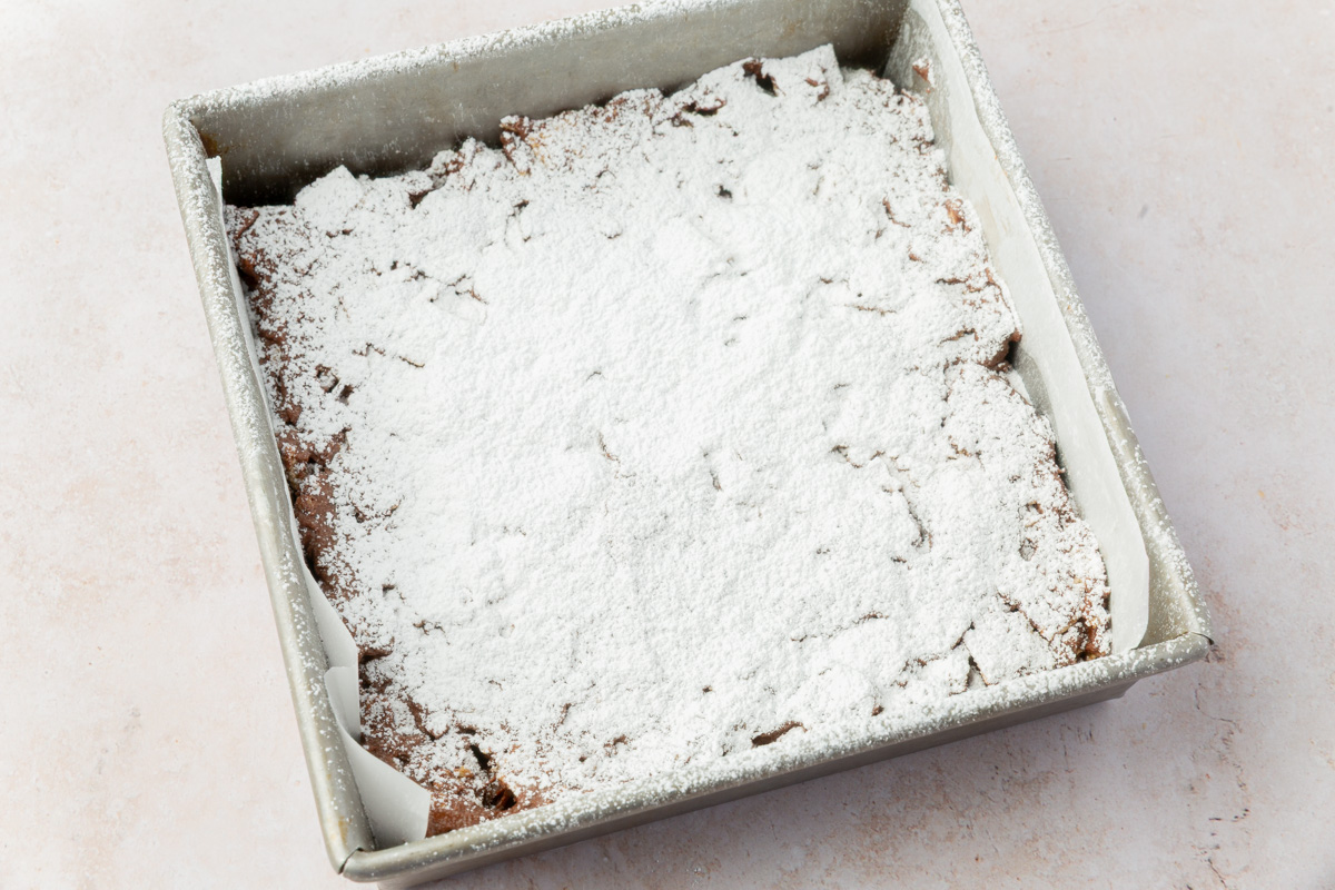 A pan of puppy chow bars fully set and generously dusted with powdered sugar.