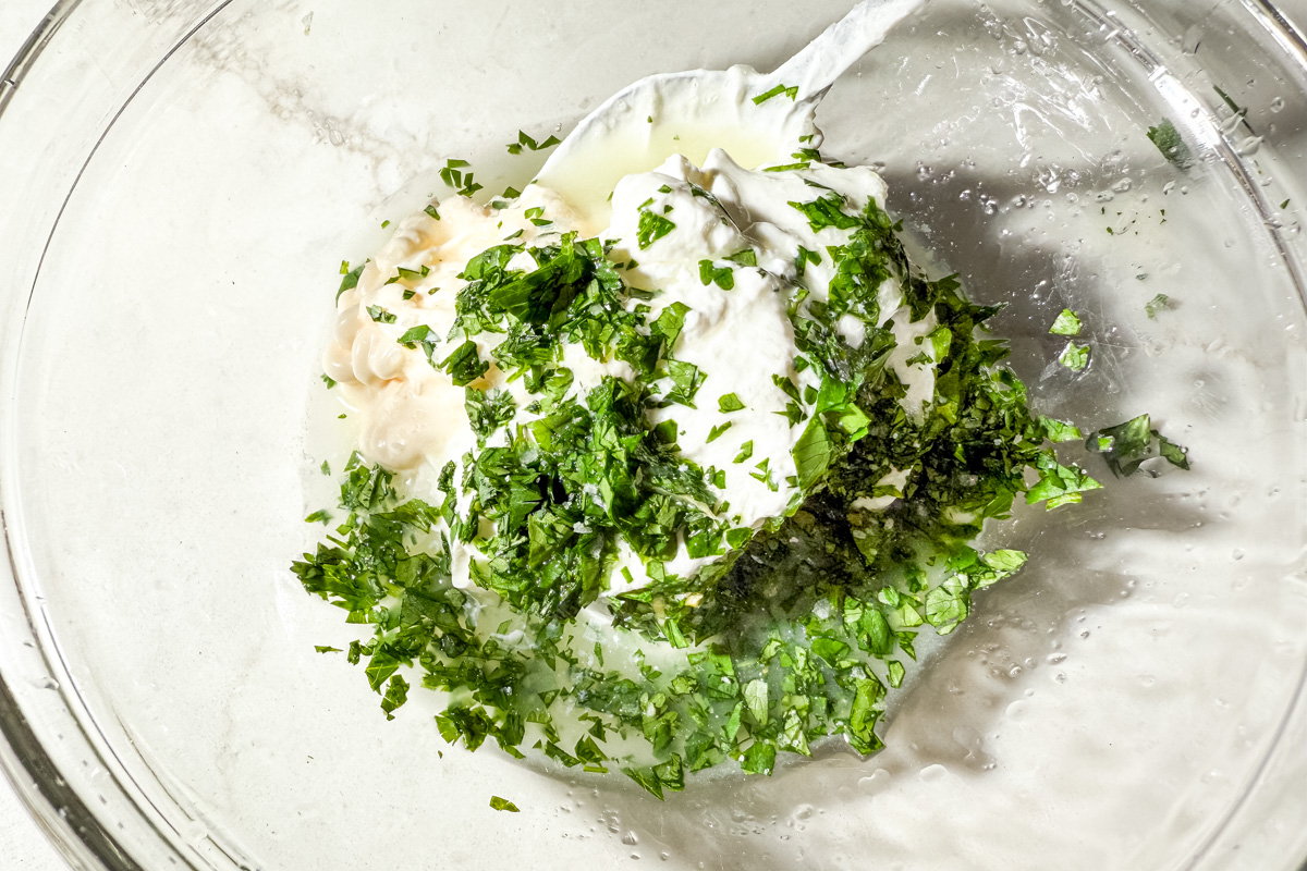 Bowl with sour cream, mayonnaise, lime juice, and chopped cilantro for creamy cilantro lime dressing.
