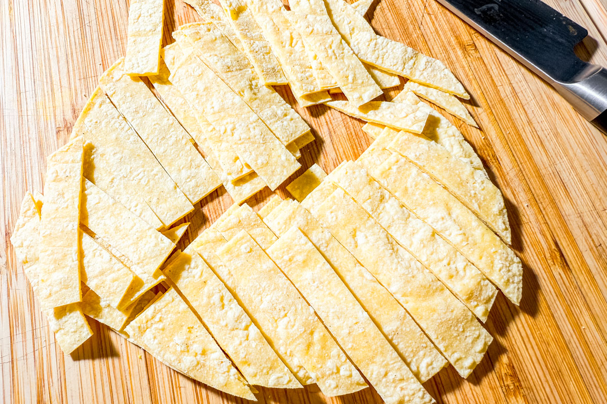 Corn tortillas cut into thin strips on a cutting board, ready to fry for taco salad.