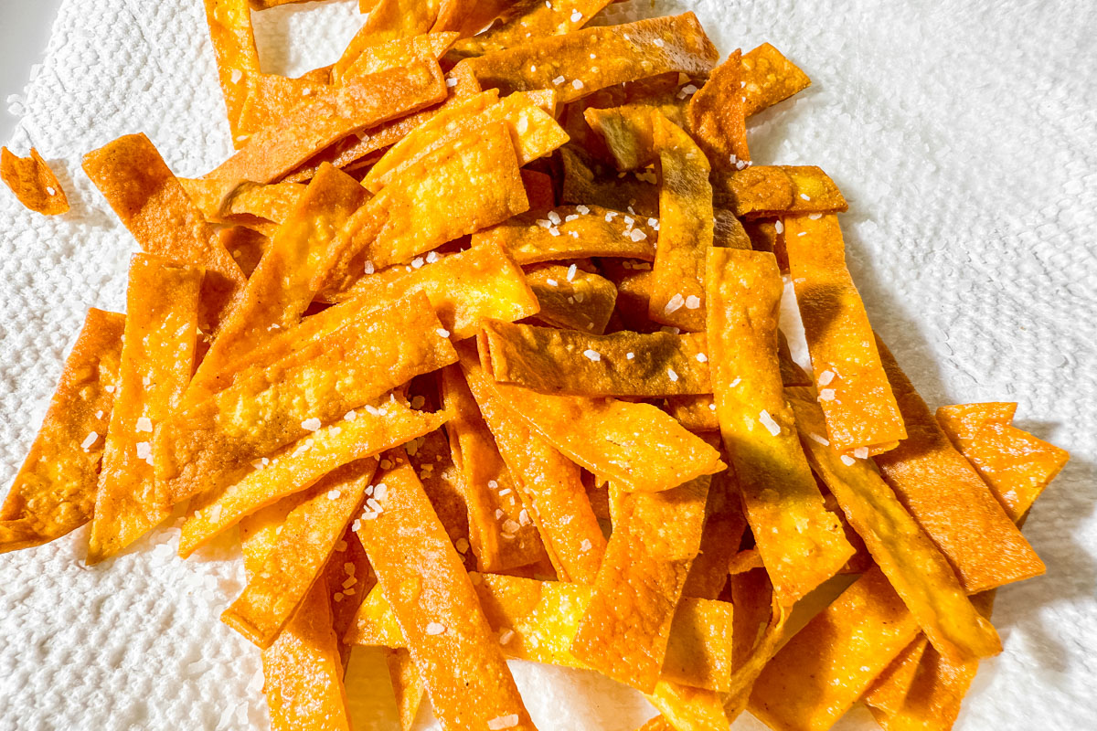 Golden fried corn tortilla strips sprinkled with salt, draining on paper towel.