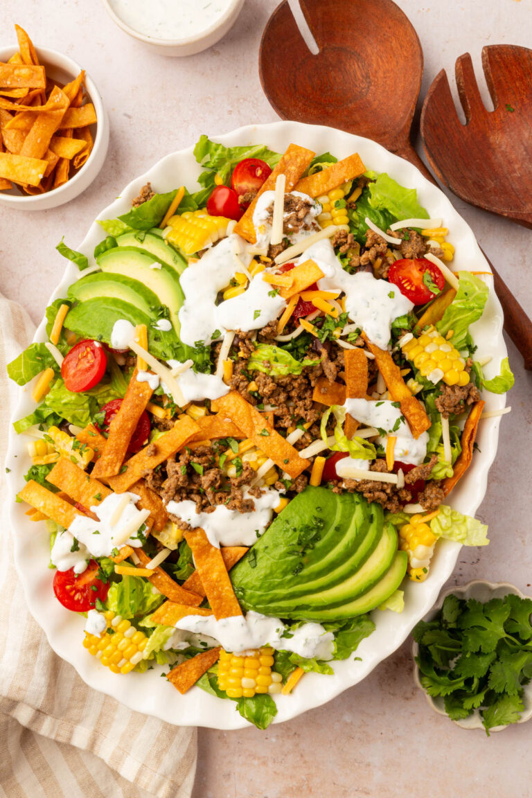 Large serving platter of gluten-free taco salad with romaine, beef, avocado, corn, tomatoes, cheese, and fried tortilla strips.