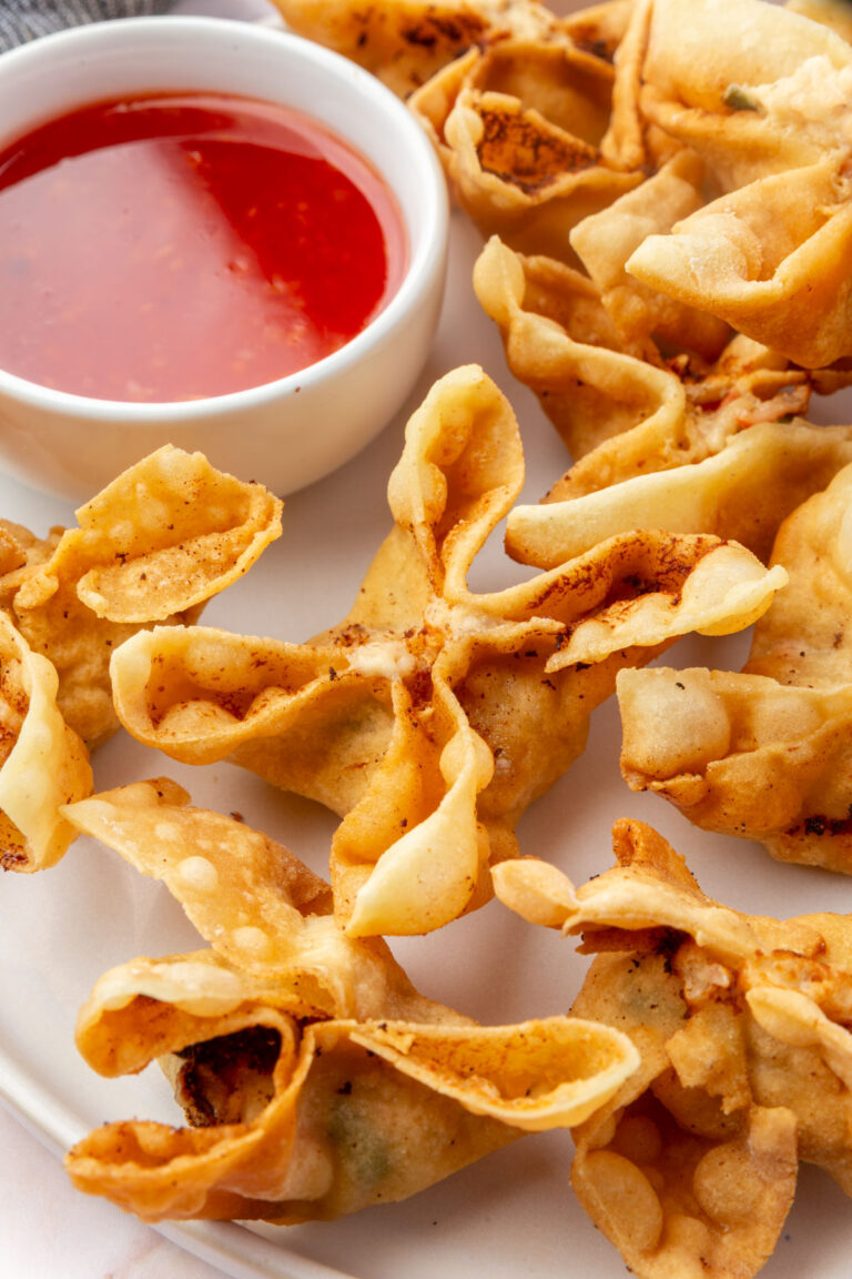 A plate of crispy gluten-free crab rangoons served with a bowl of sweet and sour dipping sauce.