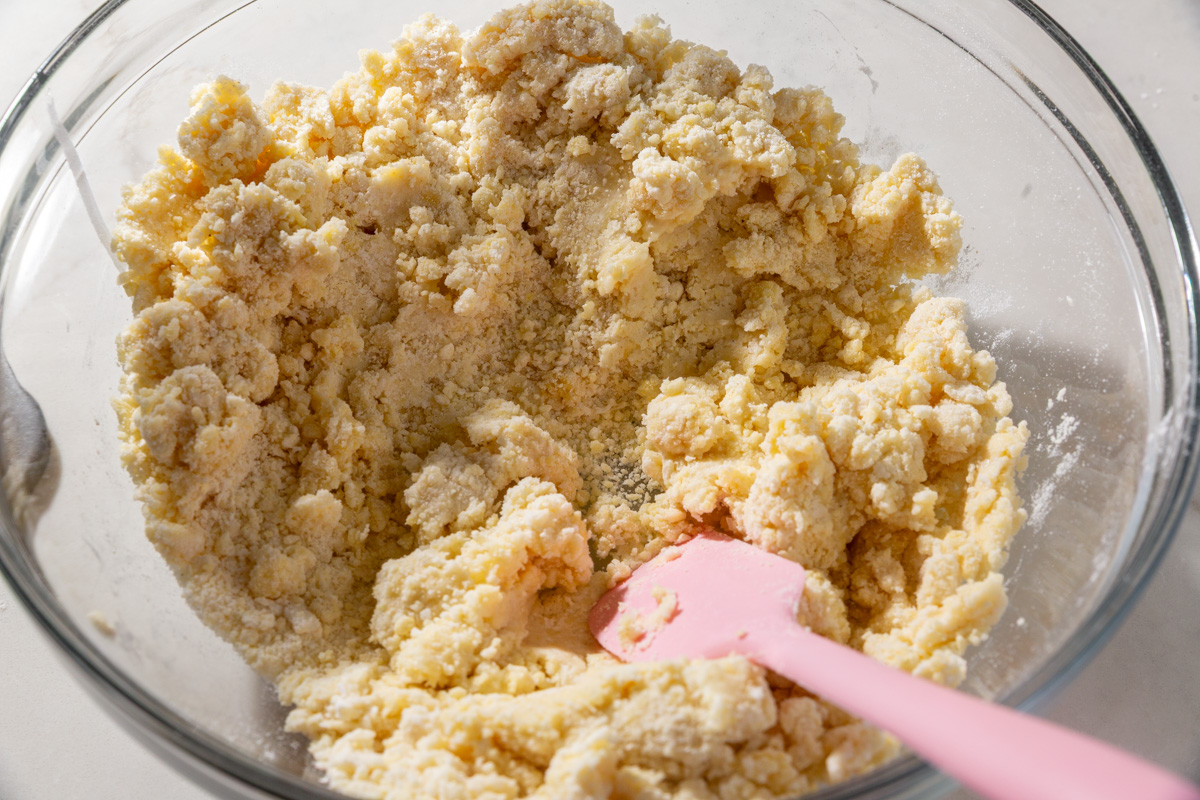 Glass bowl with crumbly gluten-free wonton dough mixture and a pink spatula.