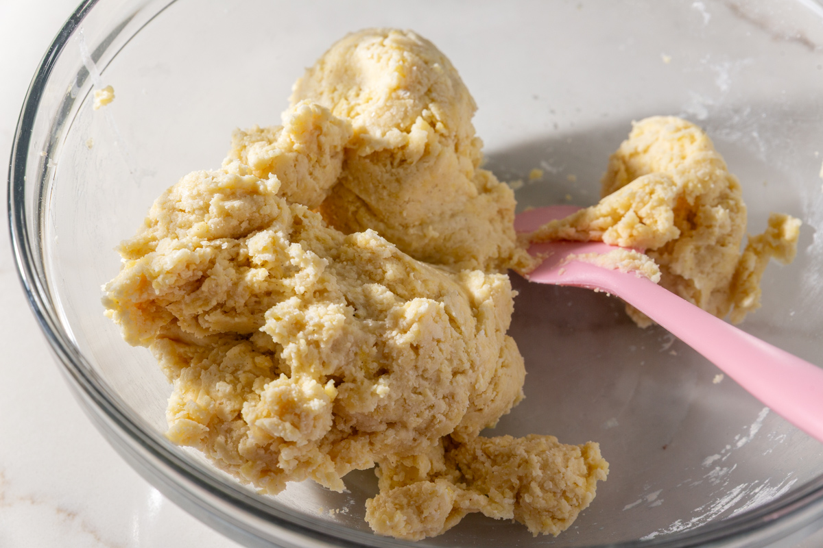 Partially kneaded gluten-free wonton wrapper dough sitting in a glass mixing bowl with a spatula.