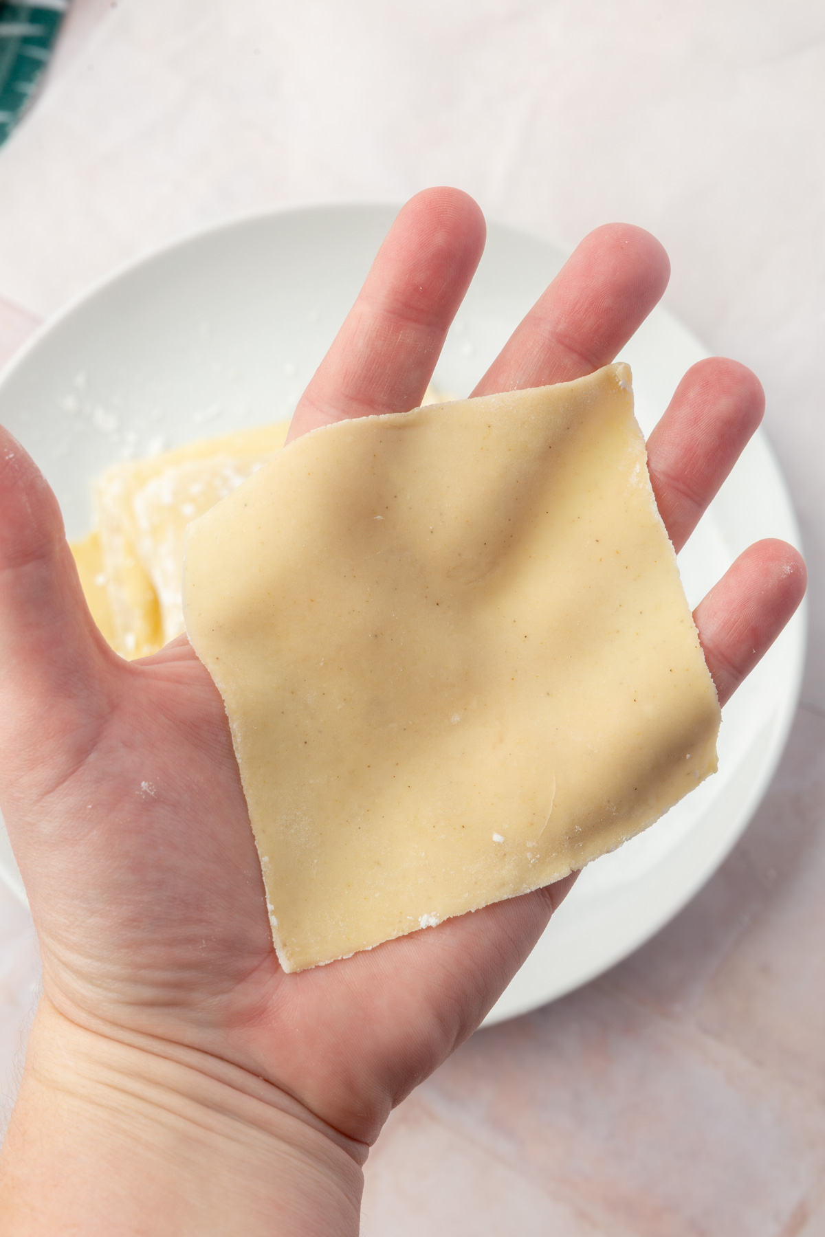 Hand holding a single homemade gluten-free wonton wrapper to show thin, flexible texture.