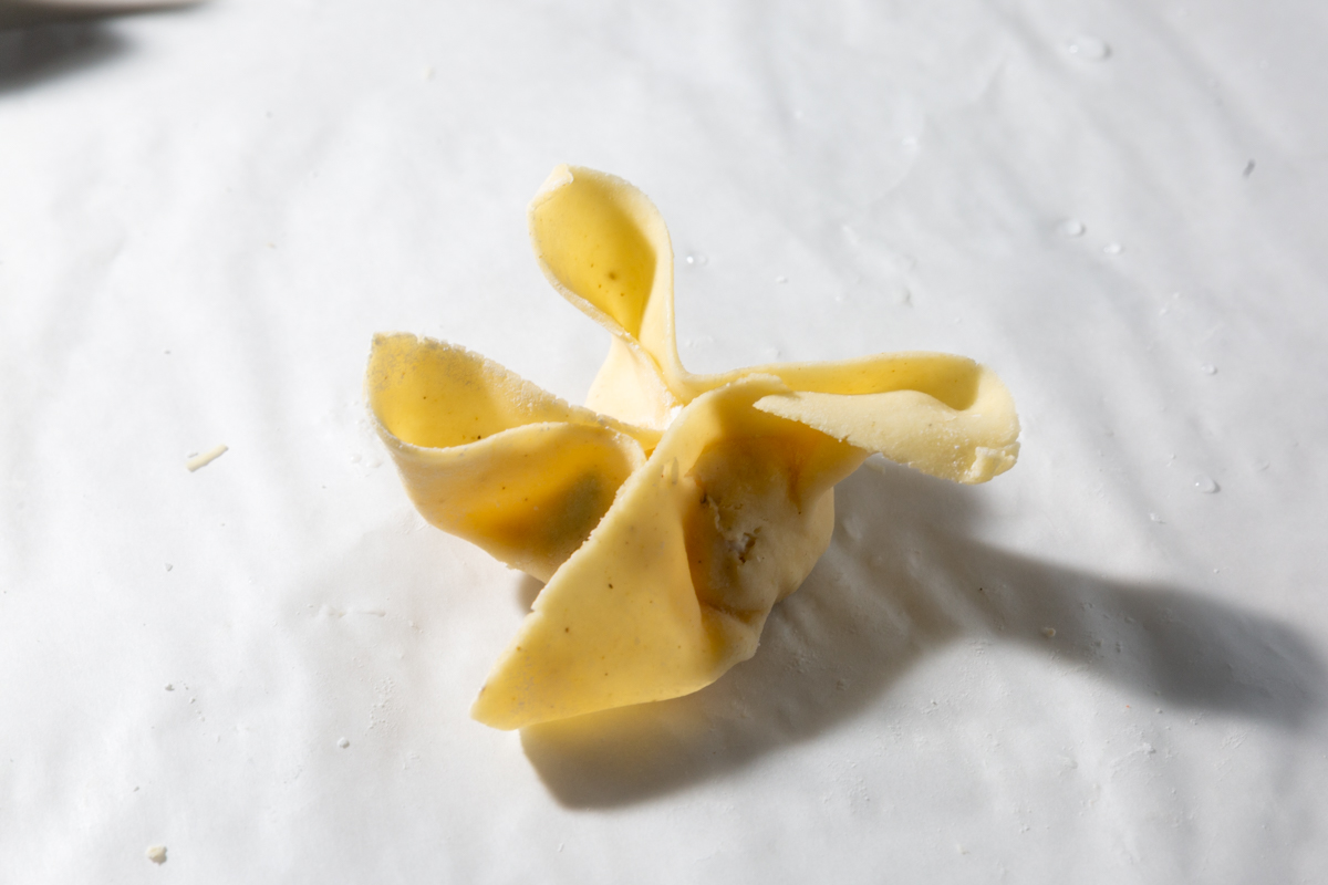 A gluten-free wonton wrapper folded around a crab rangoon filling, showing the classic pinched shape before frying.