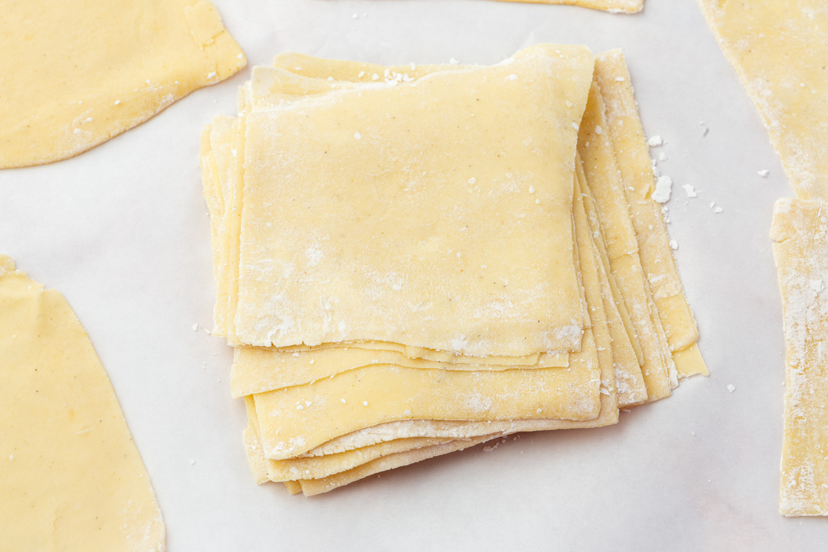 Stack of homemade gluten-free wonton wrappers lightly dusted with flour on parchment paper.