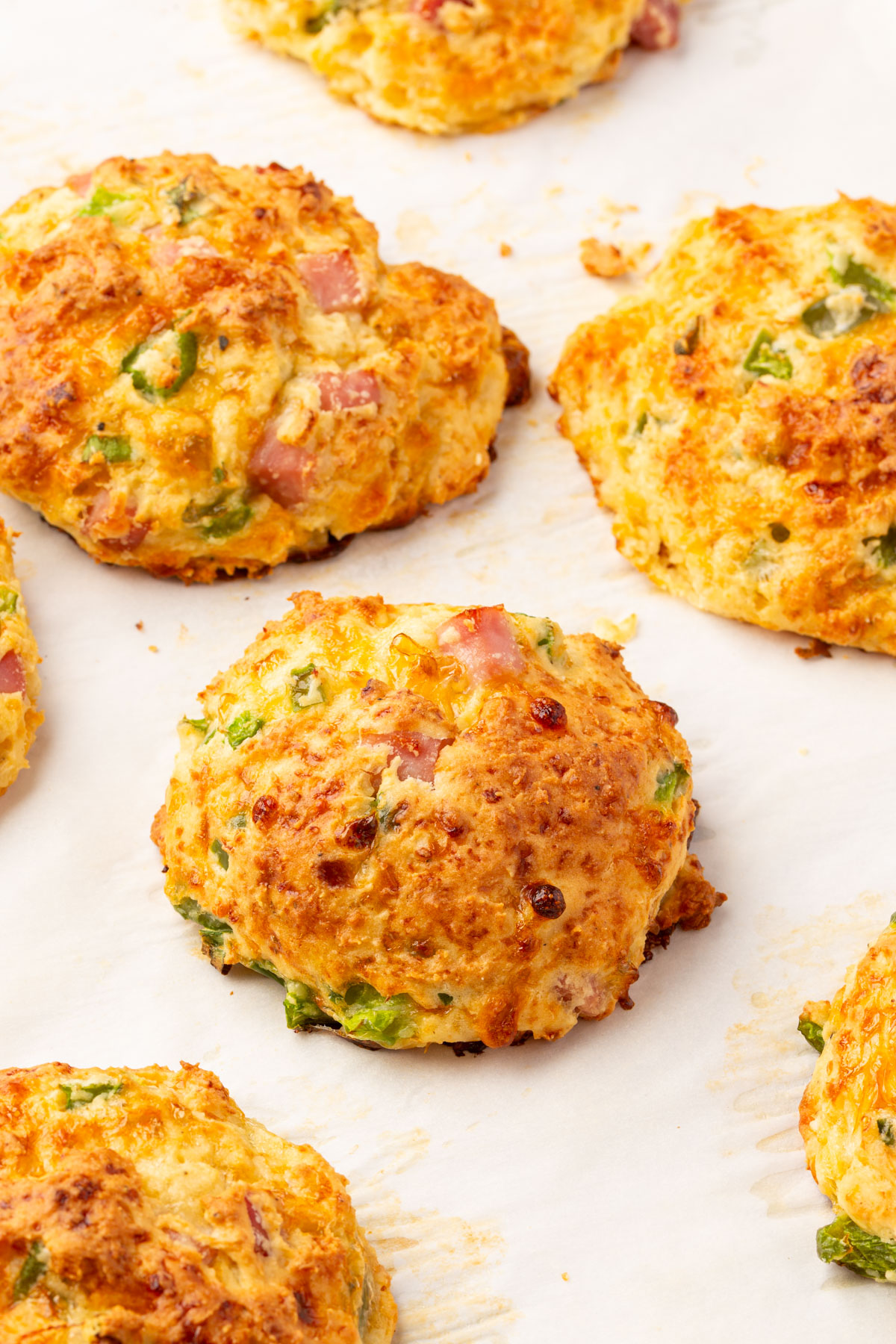 Gluten-free cottage cheese breakfast biscuits baked on parchment paper with browned tops and visible ham and vegetables.