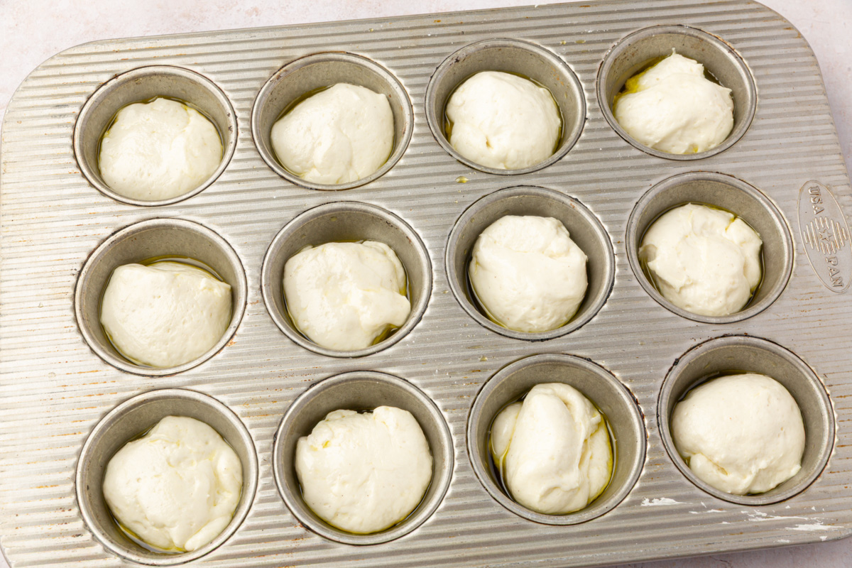 Portioned balls of gluten-free focaccia dough placed in an oiled muffin tin before rising.
