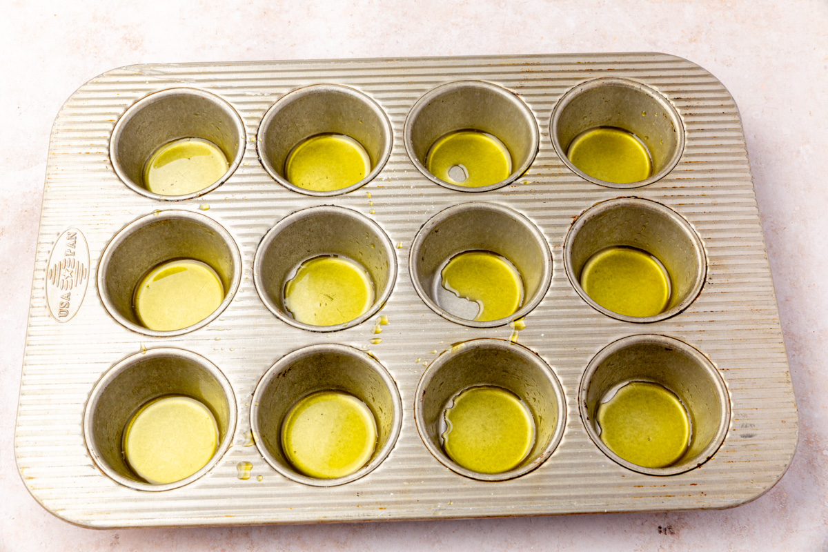 Muffin pan brushed with olive oil, ready for gluten-free focaccia dough portions.