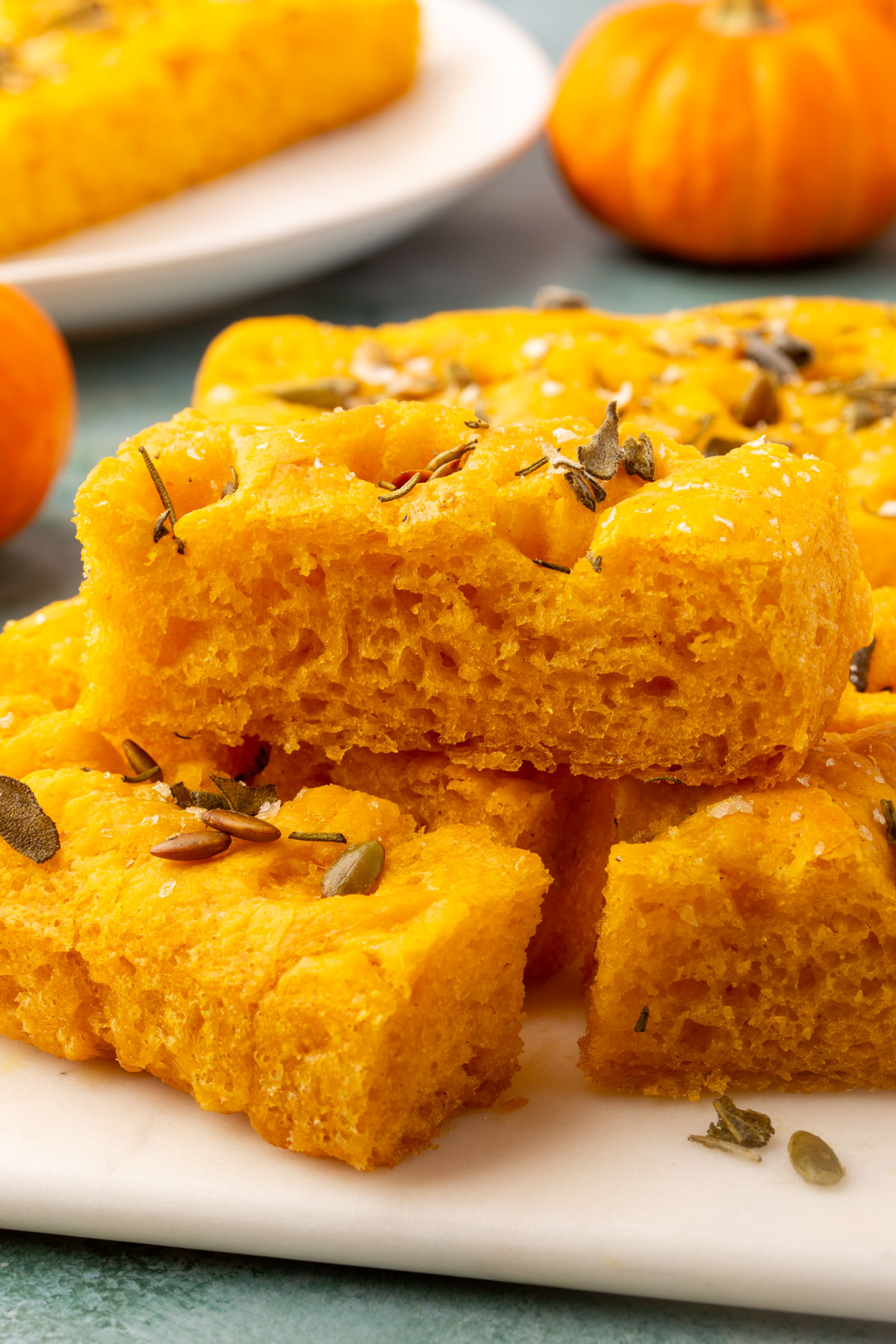 Stacked slices of gluten-free pumpkin focaccia on a marble board with mini pumpkins in the background.