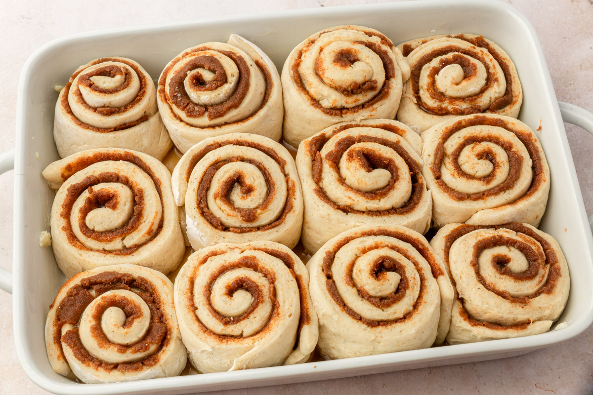 Pan of unbaked gluten-free cinnamon rolls arranged tightly in a white baking dish, showing smooth, even spirals of cinnamon filling.
