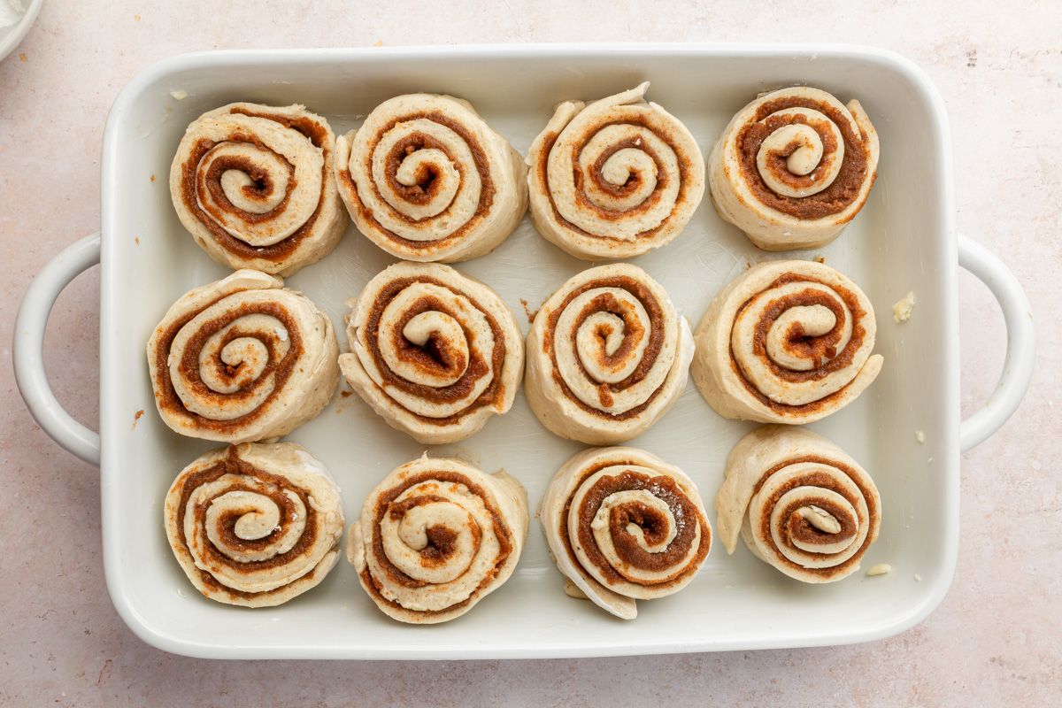 Overhead view of unbaked gluten-free cinnamon rolls in a white baking dish before proofing, showing visible cinnamon swirls.