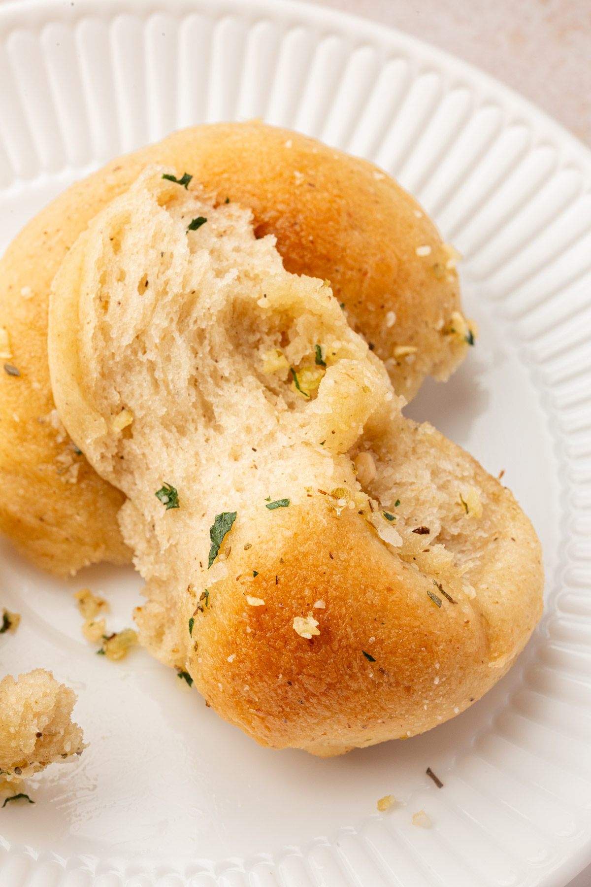 A gluten-free garlic knot torn open on a white plate, showing a soft, fluffy interior with garlic and herbs.