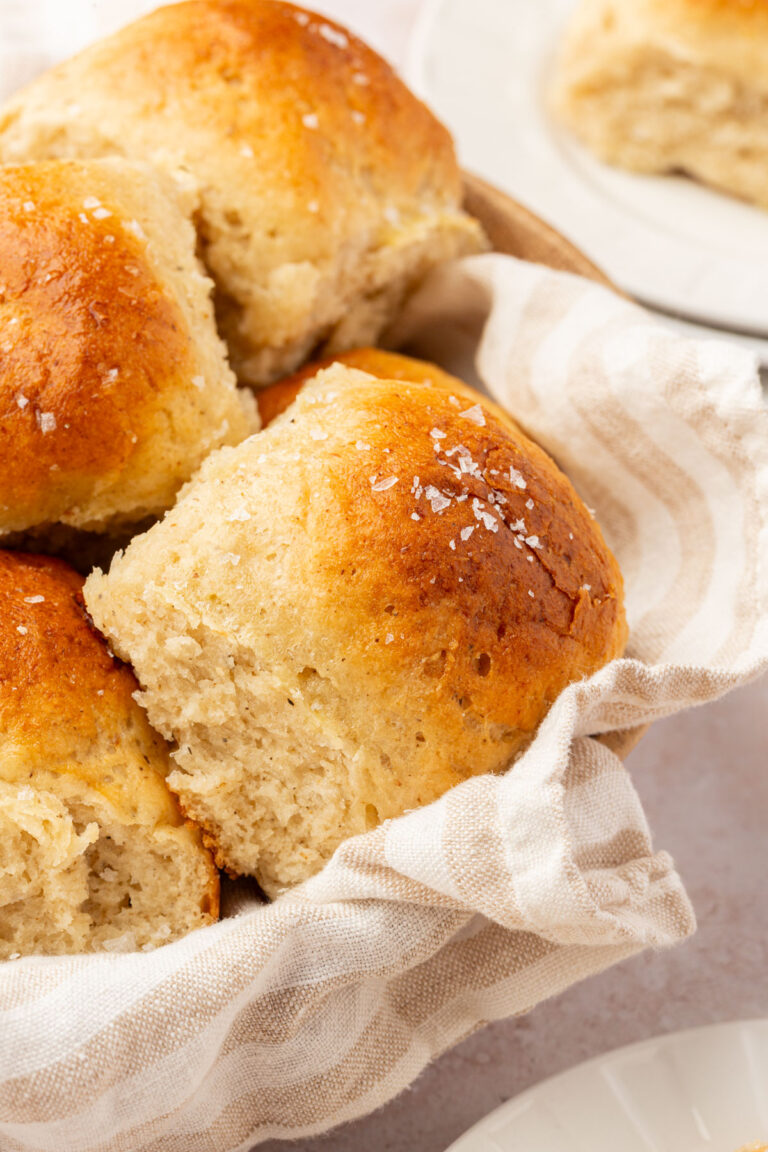 Close-up of golden gluten-free dinner rolls nestled in a striped linen basket.