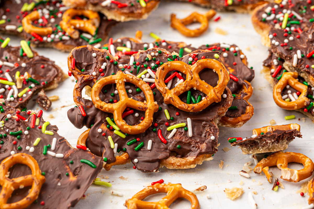Overhead view of gluten-free Christmas pretzel bark pieces scattered on white surface showing chocolate coating, festive sprinkles, and pretzel pieces.